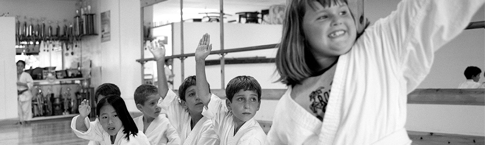 Children in gis sit in a line on the dojo floor